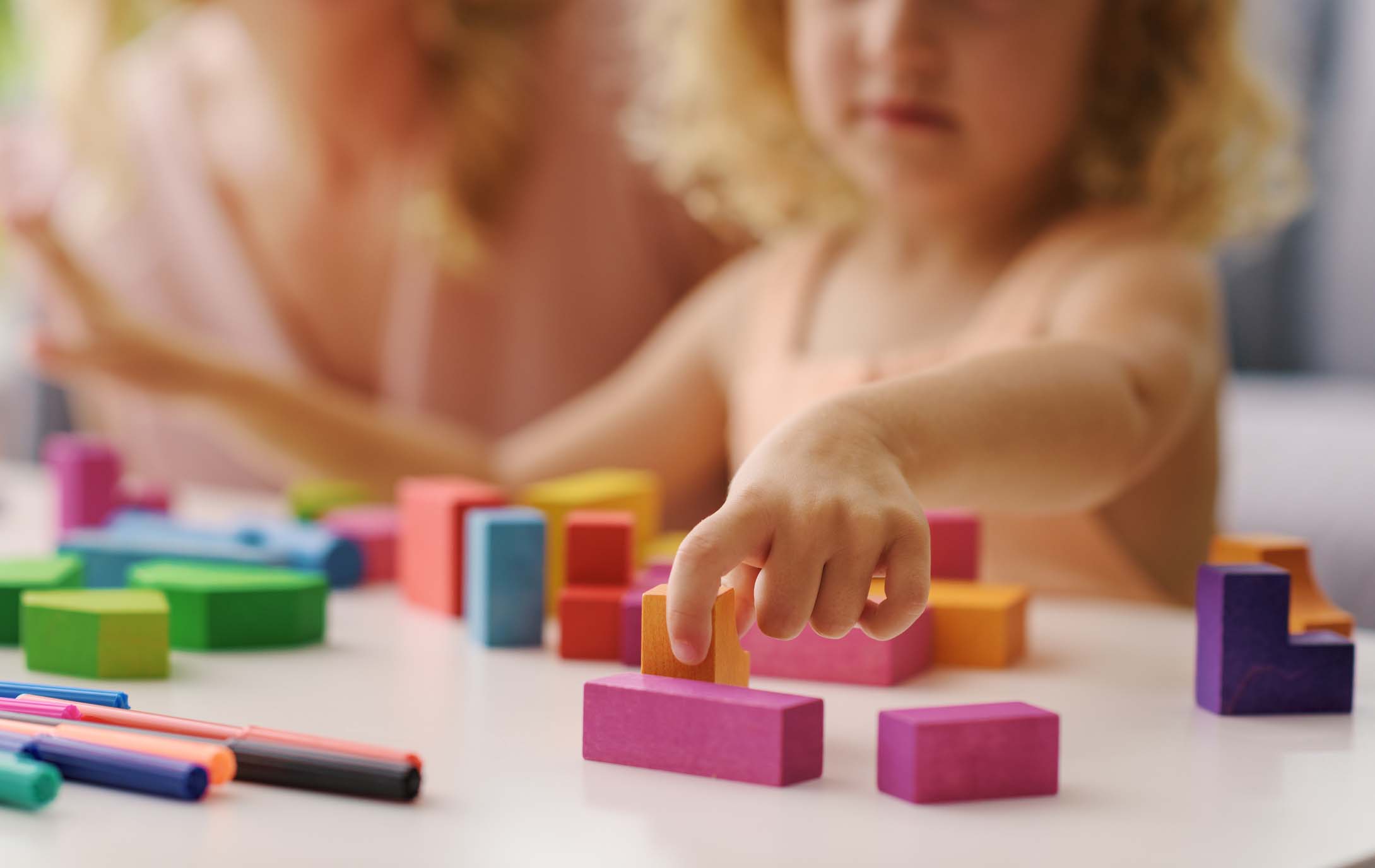 Child playing with wooden blocks, her mother is next to her, hand close up Child playing with wooden blocks, her mother is next to her, hand close up